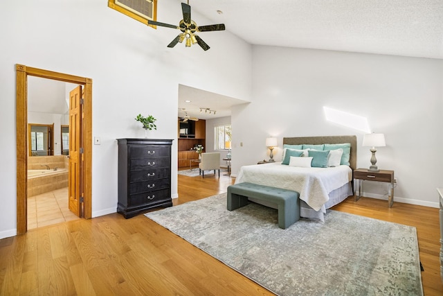 bedroom featuring wood finished floors, baseboards, ensuite bath, high vaulted ceiling, and ceiling fan
