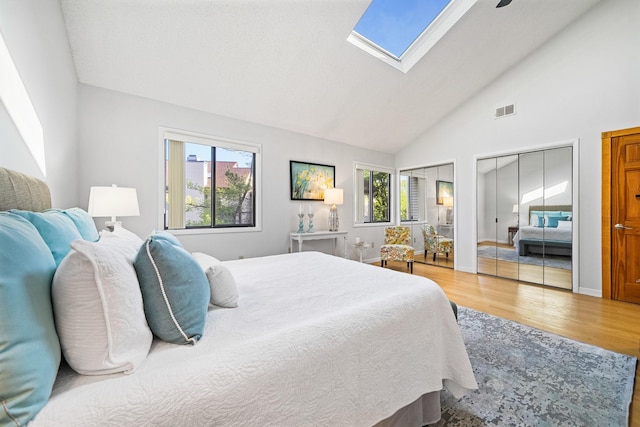 bedroom featuring multiple closets, light wood-style flooring, multiple windows, a skylight, and high vaulted ceiling