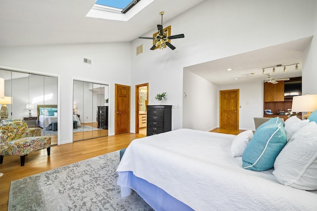 bedroom featuring two closets, light wood-type flooring, a skylight, a ceiling fan, and high vaulted ceiling