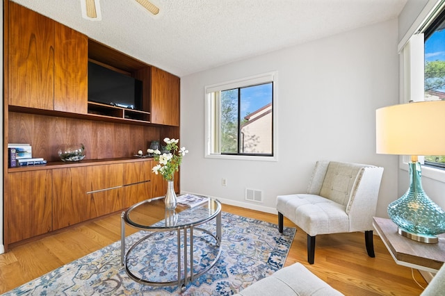 living area featuring plenty of natural light, light wood-style flooring, a textured ceiling, and a ceiling fan