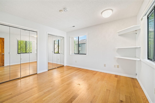unfurnished bedroom featuring multiple closets, multiple windows, a textured ceiling, light wood-type flooring, and baseboards