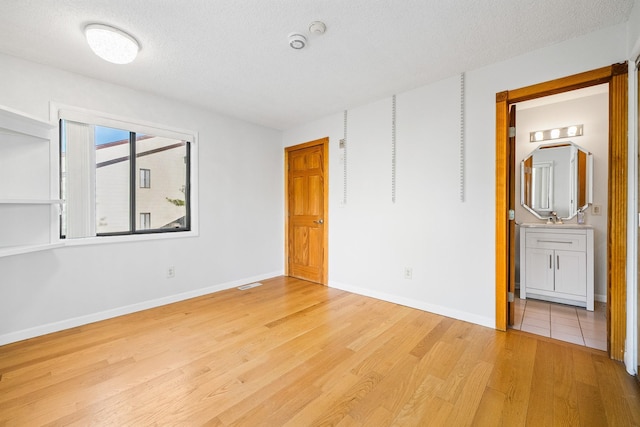 unfurnished bedroom with light wood-style floors, baseboards, a textured ceiling, and a sink