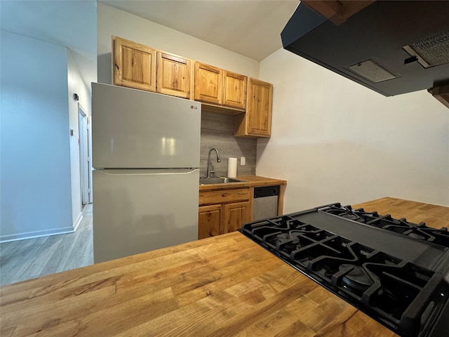 kitchen featuring freestanding refrigerator, a sink, butcher block counters, tasteful backsplash, and wood finished floors