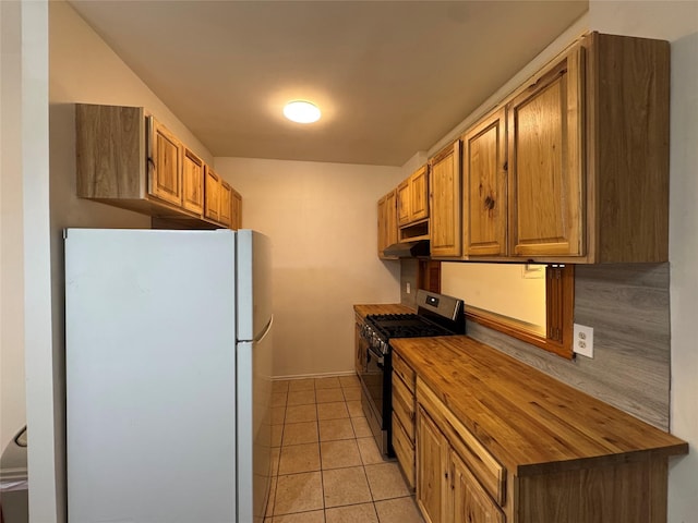 kitchen featuring freestanding refrigerator, stainless steel gas range oven, wood counters, light tile patterned floors, and baseboards