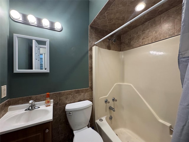 full bathroom featuring shower / bath combo, vanity, toilet, a wainscoted wall, and tile walls