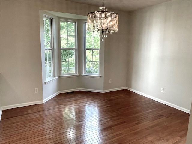 empty room with a chandelier, dark wood-style floors, and baseboards
