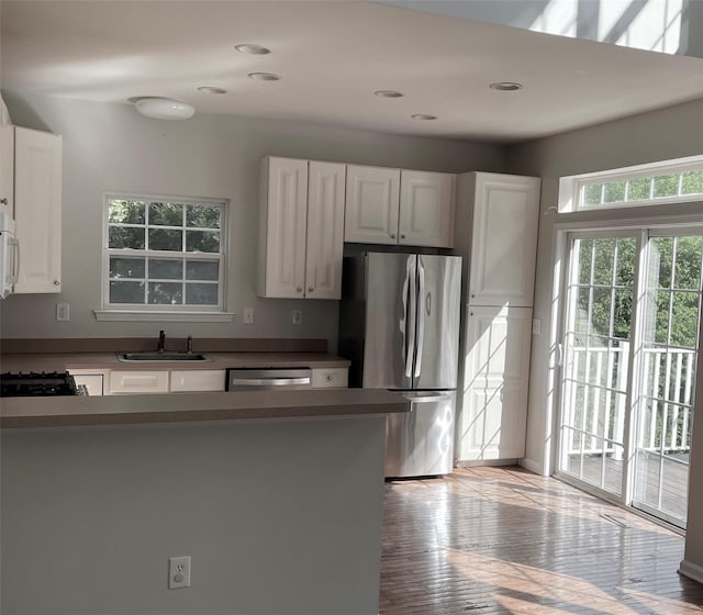 kitchen with stainless steel appliances, a sink, white cabinetry, light wood-style flooring, and recessed lighting