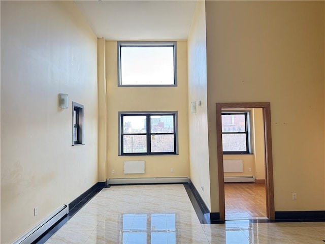 tiled empty room featuring a baseboard heating unit, a high ceiling, a baseboard radiator, and baseboards