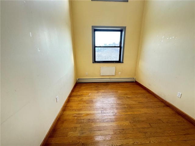 empty room featuring a baseboard heating unit, wood-type flooring, and baseboards
