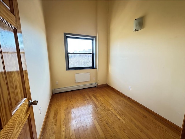 spare room featuring a baseboard heating unit, hardwood / wood-style floors, plenty of natural light, and baseboards