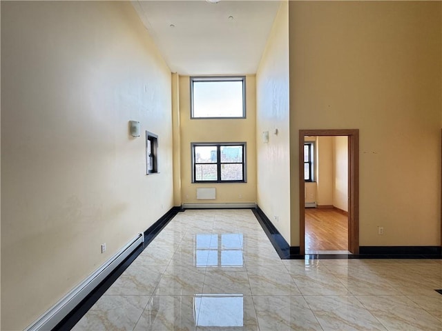 spare room featuring a high ceiling, baseboard heating, light marble finish floors, a baseboard radiator, and baseboards