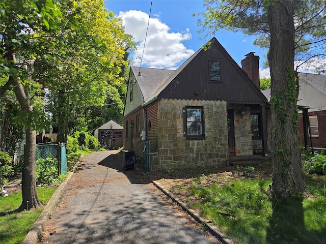 view of home's exterior featuring stone siding, fence, a chimney, and driveway