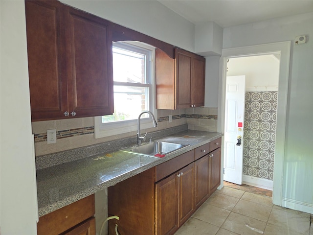 kitchen with a sink, decorative backsplash, baseboards, and dark countertops