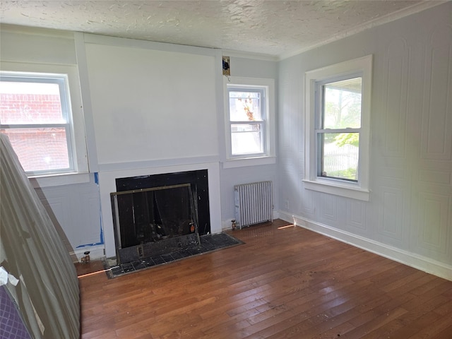 unfurnished living room featuring radiator, wood-type flooring, a textured ceiling, a fireplace with flush hearth, and ornamental molding