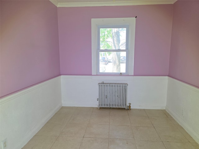 unfurnished room with radiator heating unit, a wainscoted wall, and light tile patterned floors