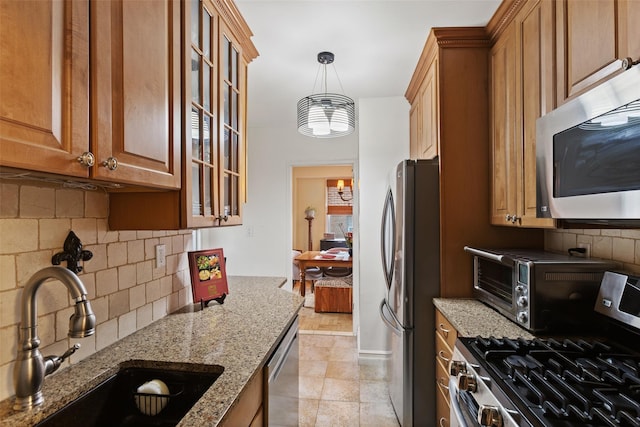kitchen with stainless steel appliances, a sink, decorative backsplash, light stone countertops, and brown cabinetry