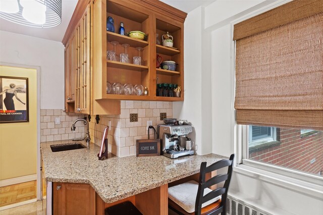 kitchen with a sink, light stone counters, tasteful backsplash, a kitchen bar, and brown cabinetry