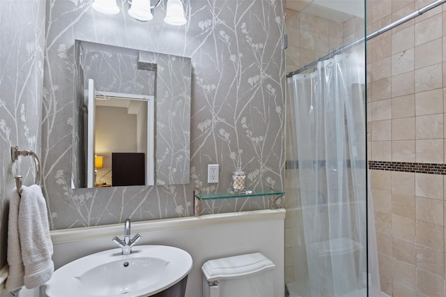 full bathroom with tiled shower, a sink, wallpapered walls, and toilet