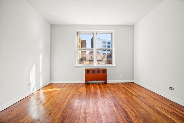 empty room with radiator, hardwood / wood-style floors, and baseboards