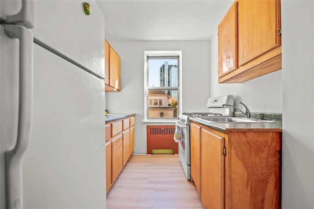 kitchen with freestanding refrigerator, stainless steel gas range oven, a sink, light wood-type flooring, and radiator