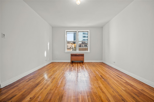 unfurnished room featuring radiator, wood finished floors, and baseboards