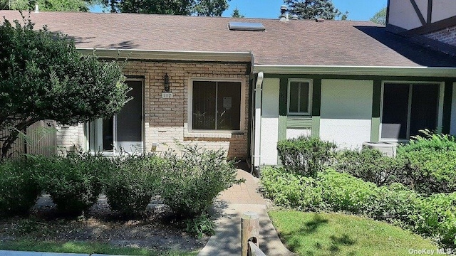 view of exterior entry with a shingled roof, stone siding, brick siding, and a porch