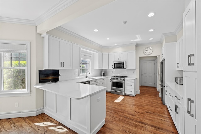 kitchen featuring stainless steel appliances, a peninsula, ornamental molding, backsplash, and white cabinetry