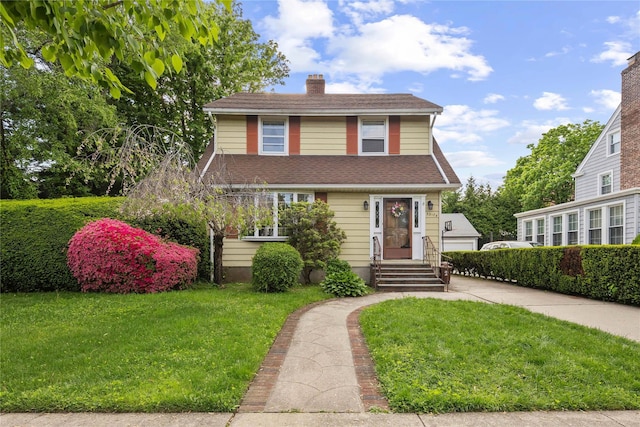view of front of home featuring a front lawn, a chimney, roof with shingles, and a detached garage