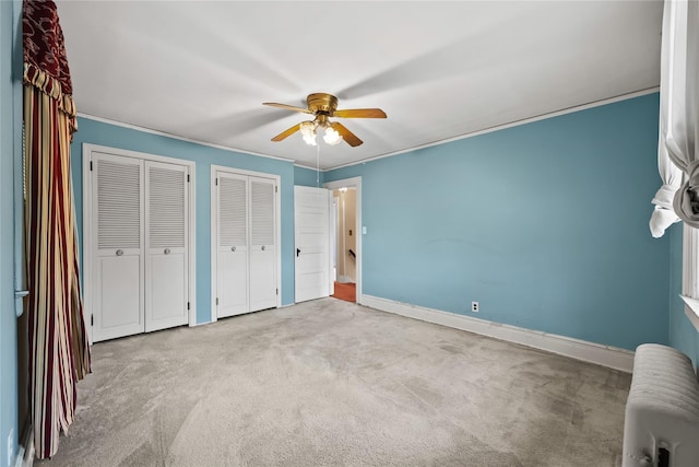 unfurnished bedroom with carpet floors, multiple closets, radiator heating unit, baseboards, and crown molding