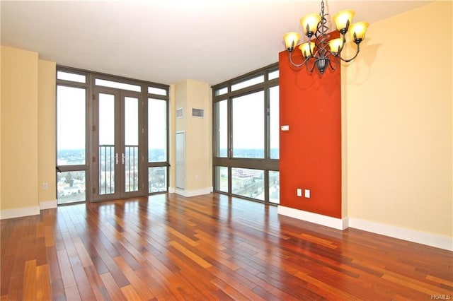 empty room with floor to ceiling windows, a chandelier, hardwood / wood-style flooring, french doors, and baseboards