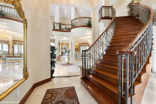 entryway with a towering ceiling, ornate columns, stairs, tile patterned flooring, and baseboards