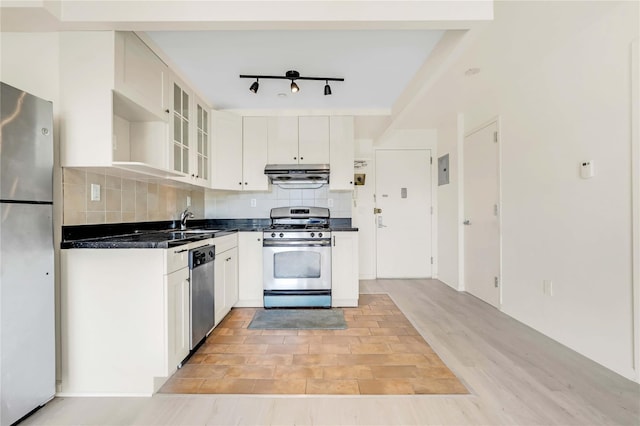 9305 37th Ave Unit 3D, Jackson Heights, NY 11372 - kitchen featuring stainless steel appliances, under cabinet range hood, dark countertops, decorative backsplash, and white cabinetry