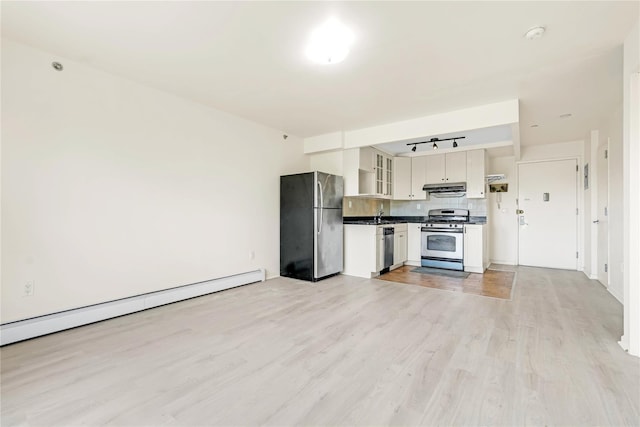 9305 37th Ave Unit 3D, Jackson Heights, NY 11372 - kitchen featuring appliances with stainless steel finishes, under cabinet range hood, dark countertops, light wood-style floors, and baseboard heating
