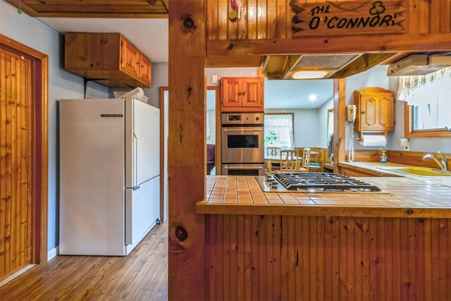 57 Empire Dr, Patterson, NY 12563 - kitchen with stainless steel appliances, a sink, tile counters, light wood-type flooring, and brown cabinetry