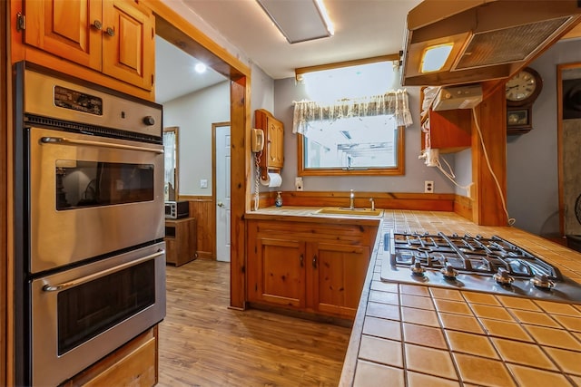 57 Empire Dr, Patterson, NY 12563 - kitchen featuring tile countertops, stainless steel appliances, a sink, brown cabinetry, and light wood-style floors