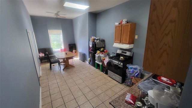 kitchen featuring stainless steel gas stove, light tile patterned floors, extractor fan, ceiling fan, and freestanding refrigerator