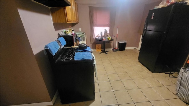 kitchen featuring freestanding refrigerator, light tile patterned flooring, brown cabinetry, and baseboards