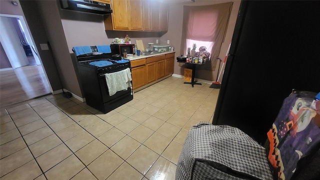 kitchen featuring black range with gas stovetop, light tile patterned floors, under cabinet range hood, light countertops, and a sink