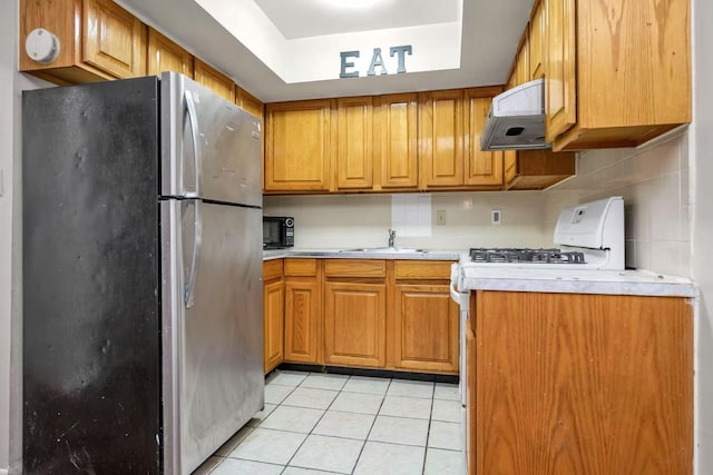 4016 E Tremont Ave, Bronx, NY 10465 - kitchen featuring freestanding refrigerator, under cabinet range hood, white gas range oven, light tile patterned floors, and light countertops