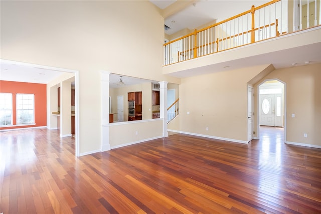 33 Avolet Ct, Mount Sinai, NY 11766 - unfurnished living room featuring a towering ceiling, wood-type flooring, ornate columns, baseboards, and stairs