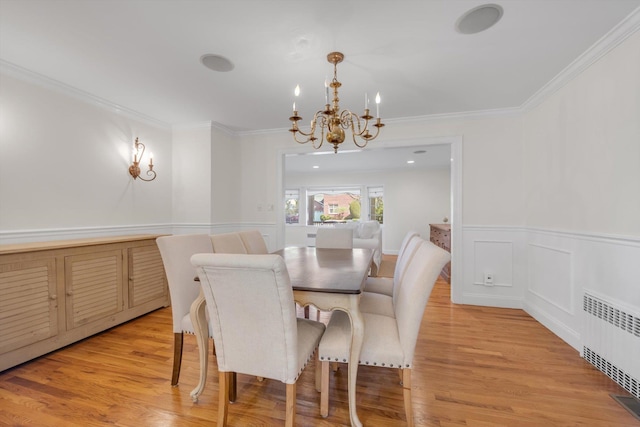 dining room featuring a chandelier, radiator, ornamental molding, light wood-style flooring, and a wainscoted wall
