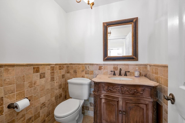 half bath with tile walls, wainscoting, toilet, and vanity