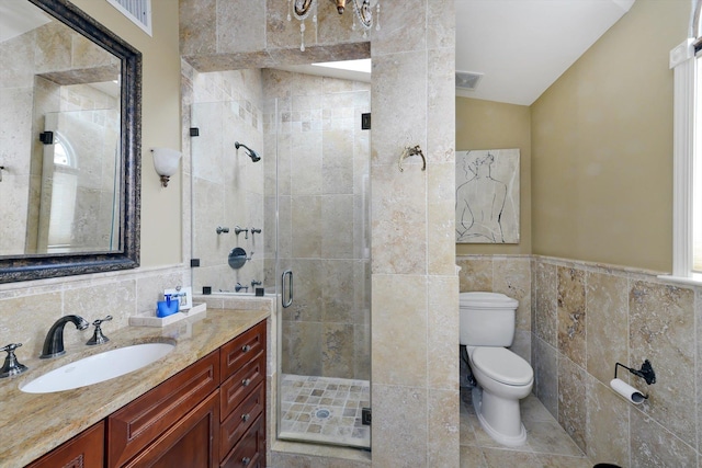 full bathroom featuring tile walls, a shower stall, toilet, vanity, and a wainscoted wall