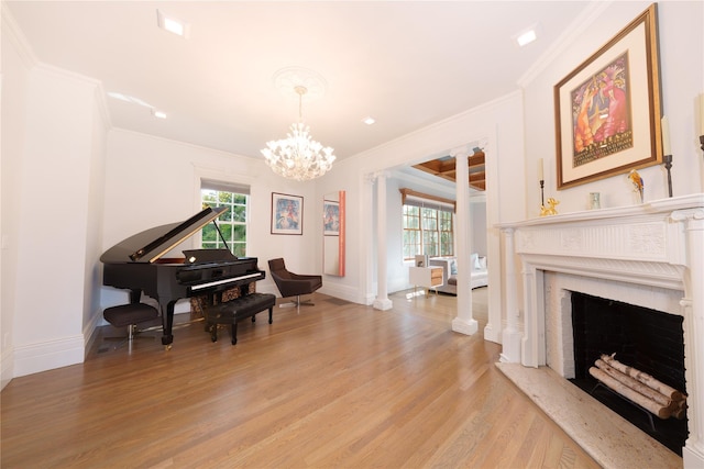 sitting room with crown molding, light wood-type flooring, a chandelier, a fireplace with raised hearth, and baseboards