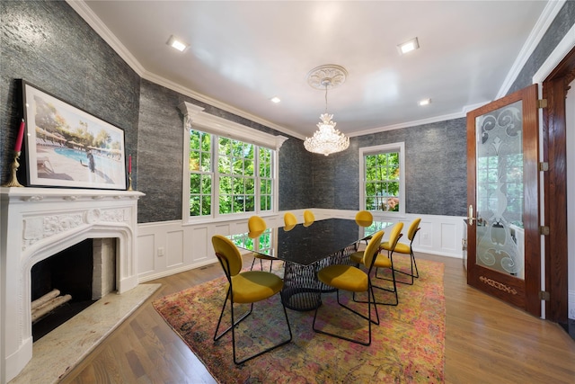 dining room featuring crown molding, a chandelier, a decorative wall, wood finished floors, and wainscoting