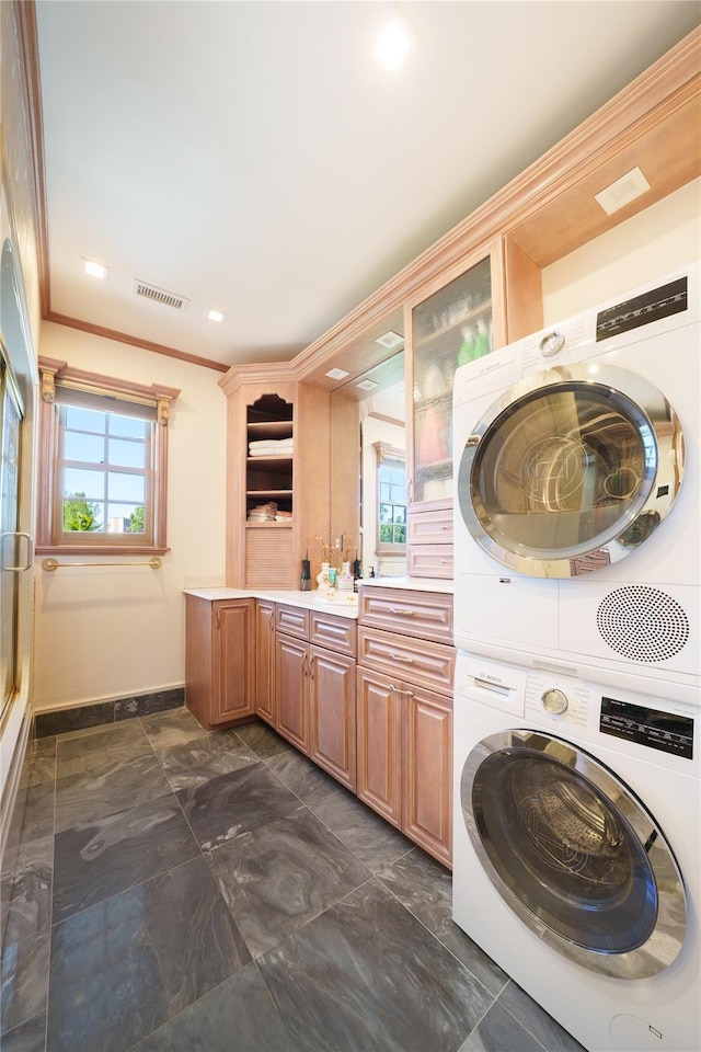 laundry area with stacked washer and clothes dryer, crown molding, cabinet space, baseboards, and dark marble finish flooring