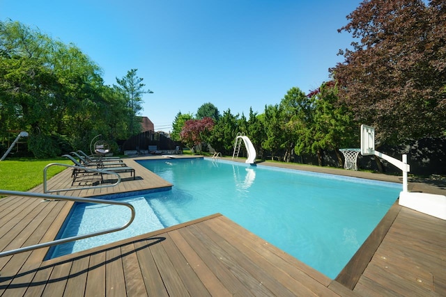 outdoor pool featuring a water slide, a wooden deck, and view of wooded area
