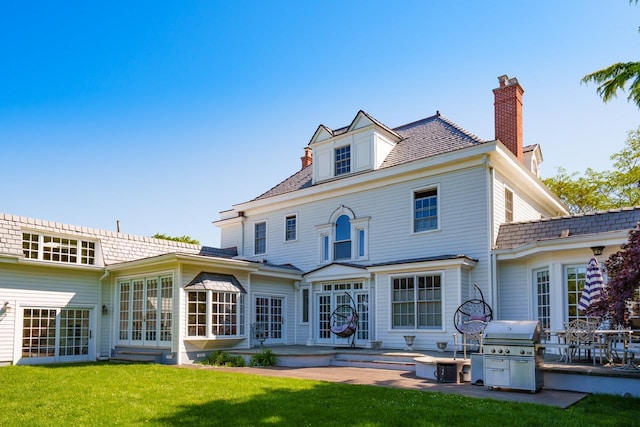 back of property with a chimney, french doors, a patio, and a lawn