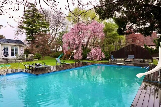 swimming pool featuring a water slide, a lawn, a patio, and a wooden deck