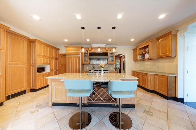 kitchen featuring under cabinet range hood, a large island, decorative backsplash, a breakfast bar area, and light stone countertops